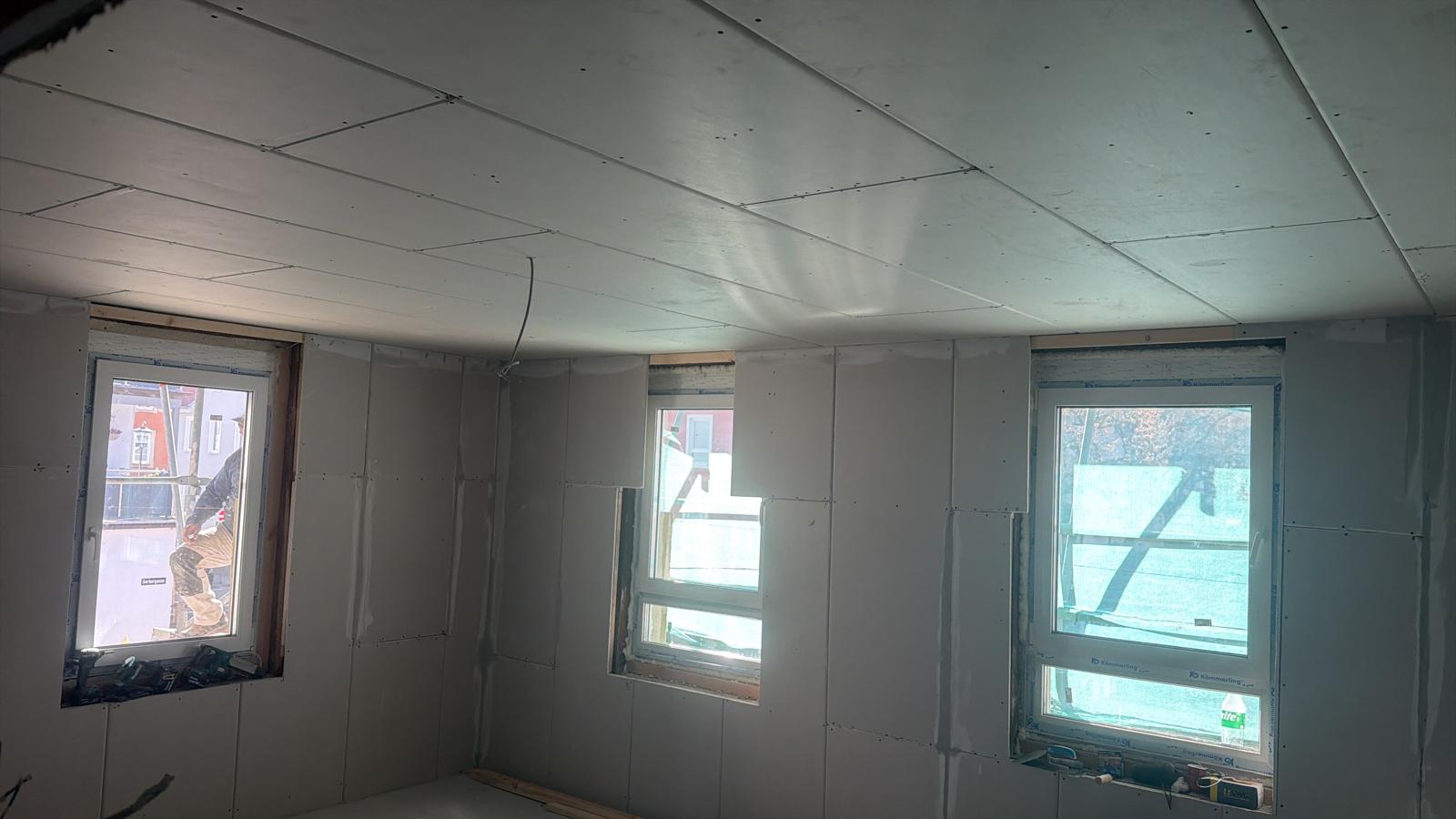 Raum mit fertig beplankten Trockenbauwänden und Decke, mehrere Fenster